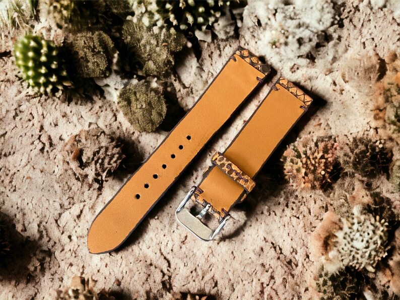 May include: Two brown leather watch straps with a textured pattern. The straps have stitching around the edges and are laid out on a textured surface.