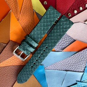 May include: A dark green watch strap with a textured, scale-like pattern and a silver buckle. The strap is displayed against a colorful background of various leather swatches in shades of orange, red, and blue.