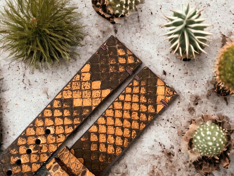 May include: Two brown leather watch straps with a snakeskin pattern and gold accents. The straps are laid out on a light gray surface.