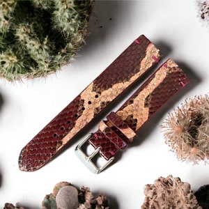 May include: A watch strap made of brown and red snakeskin with a silver buckle.