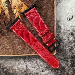 Könnte beinhalten: Zwei rote Lederarmbänder mit weißen Nähten und schwarzen Metallschließen. Die Armbänder haben ein strukturiertes, geprägtes Muster.