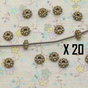 May include: A close-up of 20 antique gold-toned metal beads with a decorative flower design. The beads are strung on a brown cord. The text "X 20" is visible in the image.