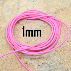 May include: A close-up of a pink elastic cord, coiled on a light brown surface. The cord is 1 mm thick.