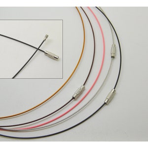 Puede incluir: Un conjunto de seis collares finos de metal de diferentes colores con cierres plateados. Los collares están dispuestos en semicírculo sobre un fondo blanco.