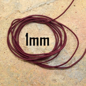 May include: A close-up of a spool of 1mm thick burgundy elastic cord. The cord is wound tightly and the end of the cord is visible.