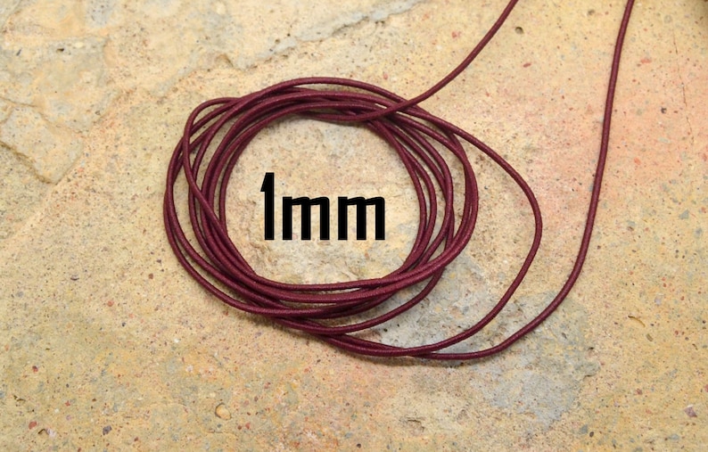 May include: A close-up of a spool of 1mm thick burgundy elastic cord. The cord is wound tightly and the end of the cord is visible.