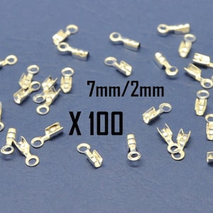 May include: A close-up of 100 silver-toned metal clasps, each measuring 7mm by 2mm. The clasps are scattered on a blue surface. The text "7mm/2mm x 100" is visible in the image.