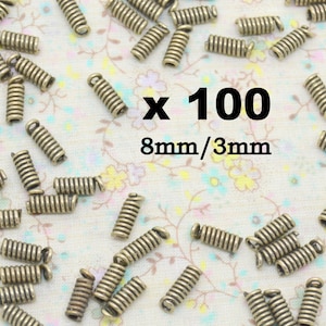 May include: A close-up of 100 antique bronze spring jump rings. Each ring measures 8mm in length and 3mm in diameter.