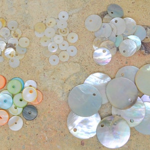 Peut inclure: Assortiment de boutons ronds en coquille de couleur blanche, irisée et multicolore avec des trous au centre. Certains boutons sont plus petits et d'autres plus grands.