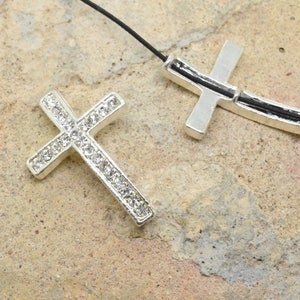 May include: Two silver cross pendants, one with clear rhinestones, the other plain, on a black cord.