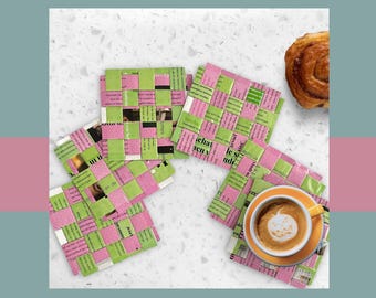 May include: Four square coasters made from woven strips of pink and green paper, with a cup of coffee on one. The coasters are arranged on a white surface, with a pastry in the background. The coffee cup is orange.