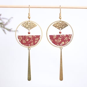 Peut inclure: Boucles d'oreilles dorées avec un cercle à motif rouge et or et une barre dorée pendante.