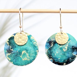 Peut inclure: Boucles d'oreilles rondes turquoise et or avec un accent en disque d'or martelé. Les boucles d'oreilles ont un aspect texturé et marbré.