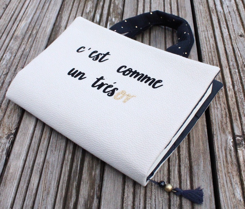 May include: A white notebook cover with black text that reads "c'est comme un tr&egrave;s bon". The cover has a black and white polka dot handle.