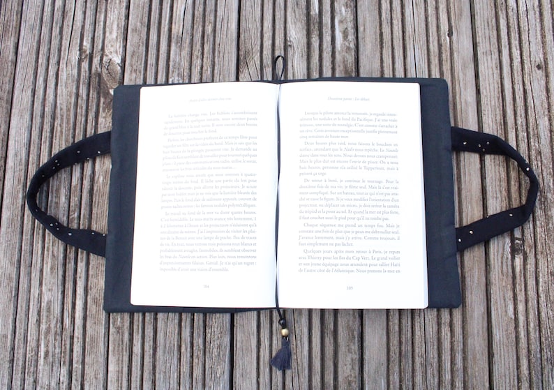 May include: A black book cover with a white bookmark and a tassel. The cover has a white polka dot pattern and two black handles.