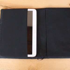 May include: A black fabric tablet case with a white tablet inside. The case has two handles and a flap that closes with a zipper.