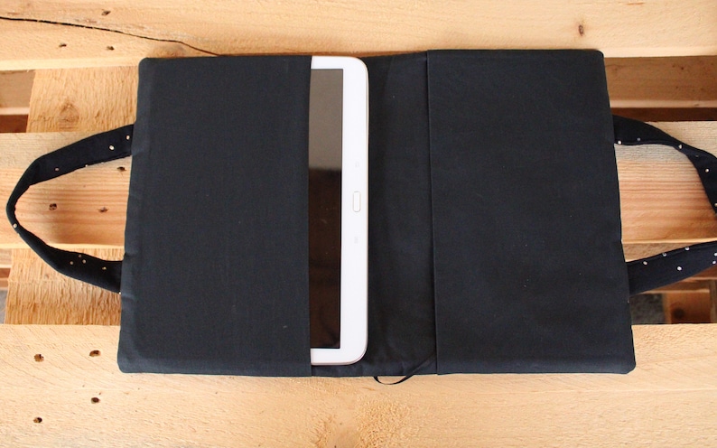 May include: A black fabric tablet case with a white tablet inside. The case has two handles and a flap that closes with a zipper.