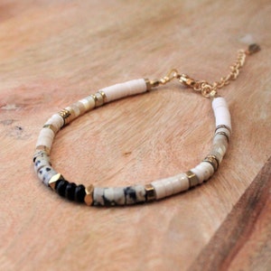 Peut inclure: Un bracelet en perles blanches et noires avec des accents dorés. Le bracelet a un fermoir doré.