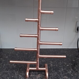 May include: A copper pipe jewelry stand with six horizontal bars for hanging jewelry. The stand is shaped like a tree and has a base with three legs.