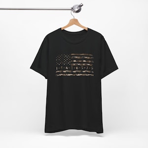 May include: A black short-sleeve t-shirt featuring a graphic of the American flag in a camouflage pattern. The flag design includes the numerical sequence 1-5-4-2-6-3-7-3 printed across the stripes in a distressed, weathered style.