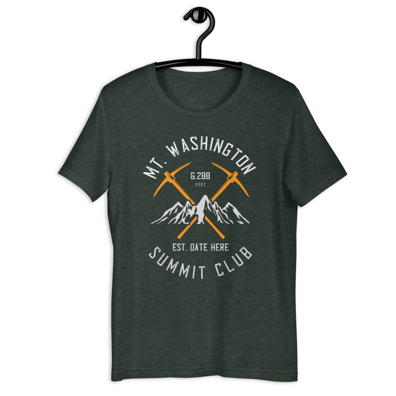 May include: A dark green t-shirt featuring a white graphic design of a mountain range with two crossed pickaxes. The text "MT. WASHINGTON 6,288 FEET EST. DATE HERE SUMMIT CLUB" is printed on the shirt.