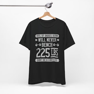 Może przedstawiać: Czarny T-shirt z białym nadrukiem, który brzmi: "99% urodzonych dzieci nigdy nie podniesie 225 funtów na ławce. Nie bądź statystyką."