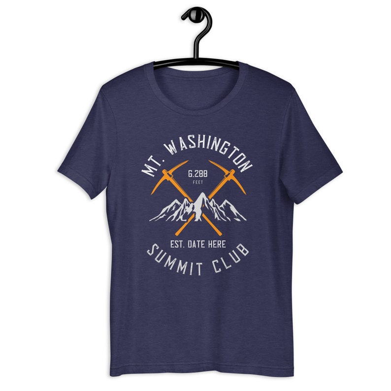 May include: A navy blue t-shirt featuring a white graphic design of a mountain range and crossed ice axes. The text "MT. WASHINGTON 6,288 FEET EST. DATE HERE SUMMIT CLUB" is printed on the shirt.