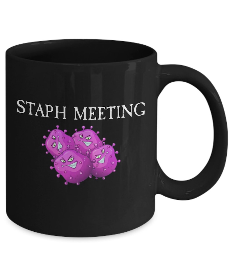 May include: Black coffee mug with the text "STAPH MEETING" in white lettering and a cartoon image of purple bacteria with angry faces.