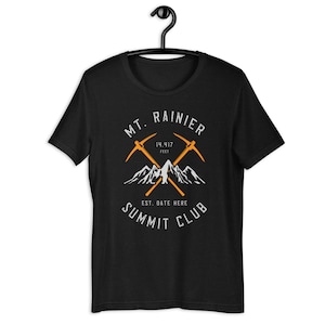 May include: Black t-shirt with a white graphic design of a mountain range with two crossed pickaxes. The text "MT. RAINIER 14,417 FEET EST. DATE HERE SUMMIT CLUB" is printed on the shirt.