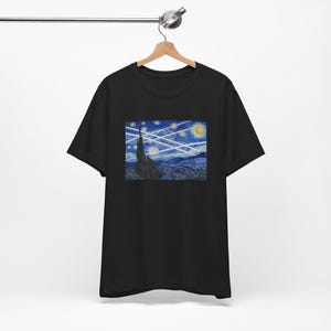 May include: Black t-shirt featuring a print of Van Gogh's "Starry Night" painting. The design includes a swirling night sky with stars, a crescent moon, and a tall, dark cypress tree. The artwork is centered on the chest.