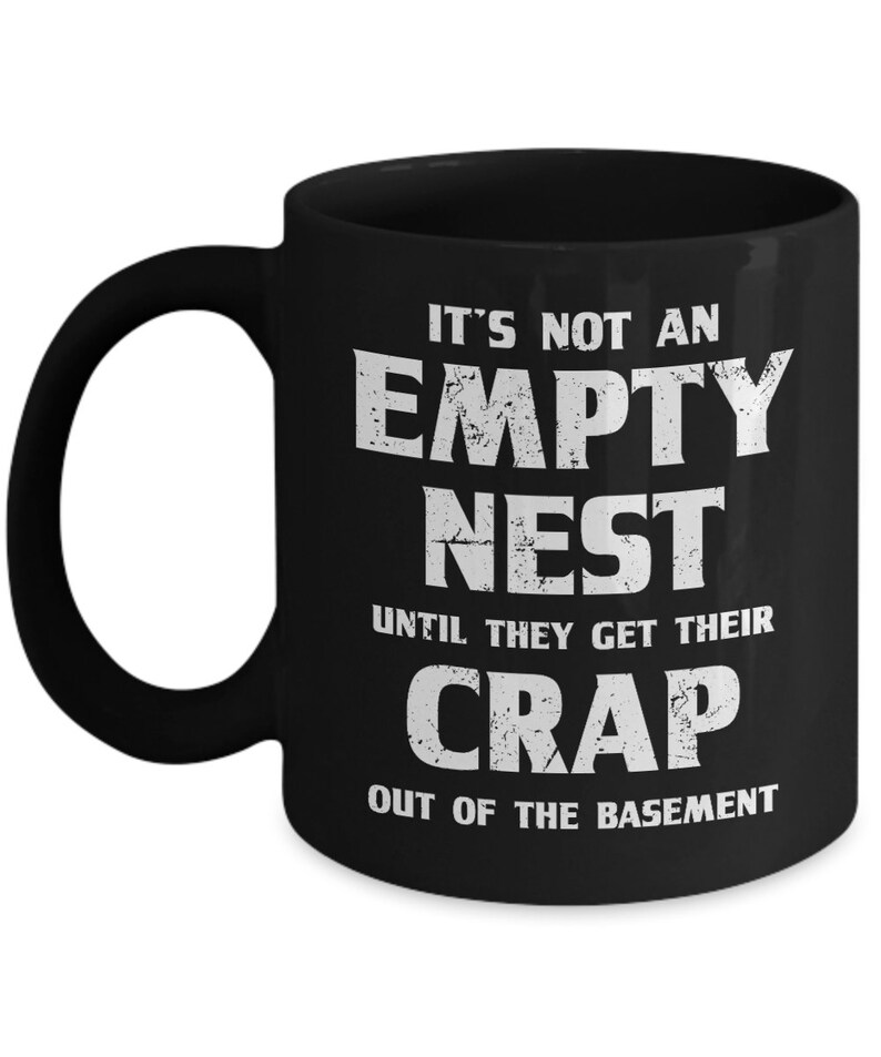 Pode incluir: Caneca de caf&eacute; de cer&acirc;mica preta com texto branco. O texto na caneca diz: "IT'S NOT AN EMPTY NEST UNTIL THEY GET THEIR CRAP OUT OF THE BASEMENT". A caneca tem uma al&ccedil;a grande e um acabamento brilhante.