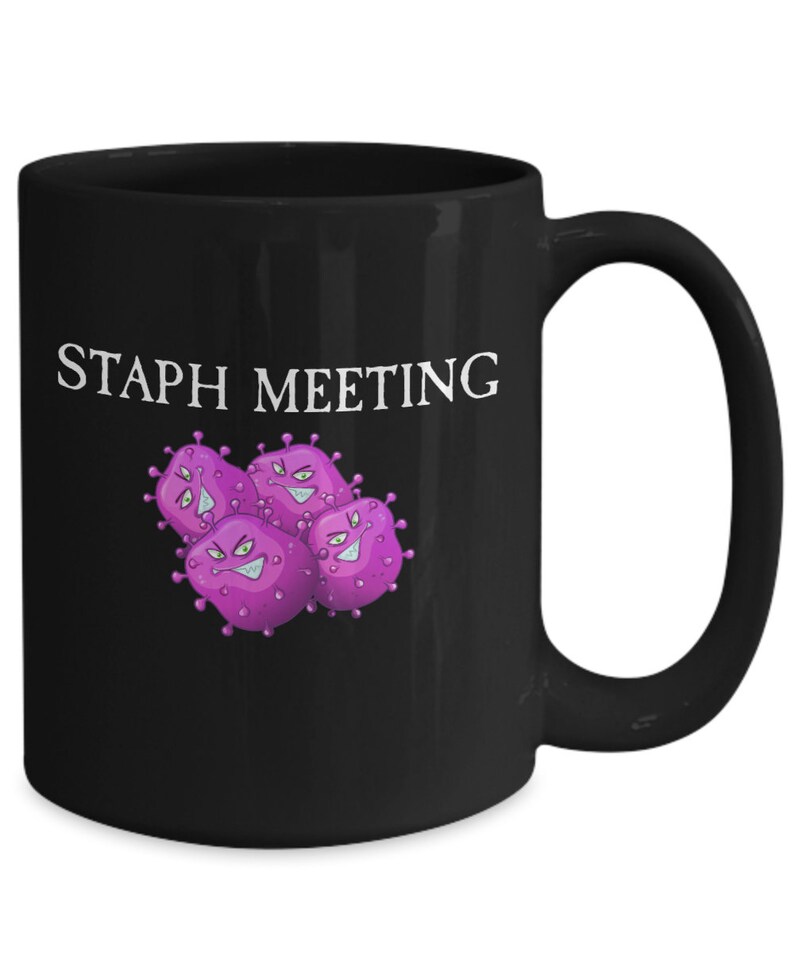 May include: Black coffee mug with the text "STAPH MEETING" in white lettering. The mug features a cartoon image of four purple bacteria with angry faces.