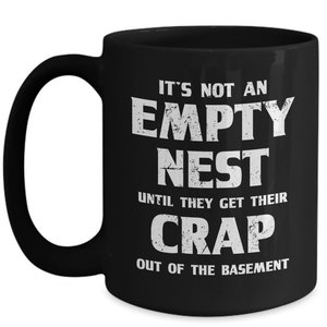 Puede incluir: Taza de cerámica negra con texto blanco: "IT'S NOT AN EMPTY NEST UNTIL THEY GET THEIR CRAP OUT OF THE BASEMENT". La taza tiene un asa grande.