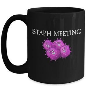 May include: Black coffee mug with a white graphic of purple cartoon bacteria and the text "Staph Meeting".