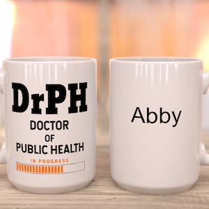May include: White ceramic coffee mug with a black design that reads "DrPH Doctor of Public Health" with a progress bar that says "In Progress". The other side of the mug has the name "Abby" in black text.