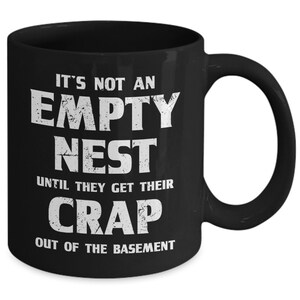 Pode incluir: Caneca de cer&acirc;mica preta com uma cita&ccedil;&atilde;o humor&iacute;stica branca: "IT'S NOT AN EMPTY NEST UNTIL THEY GET THEIR CRAP OUT OF THE BASEMENT." A caneca tem uma al&ccedil;a grande e &eacute; adequada para bebidas quentes ou frias.