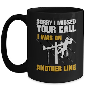 May include: Black coffee mug with a white graphic of a lineman working on a power line. The text reads "Sorry I missed your call I was on another line".