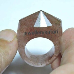 May include: A clear quartz ring with a pointed top and a reddish-brown hue. The ring is made from a single piece of quartz and has a smooth, polished finish.