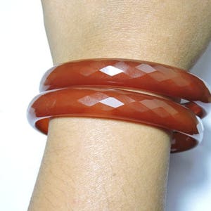 K&ouml;nnte beinhalten: Zwei braune, facettierte Armreifen, die auf dem Handgelenk einer Person &uuml;bereinander liegen.