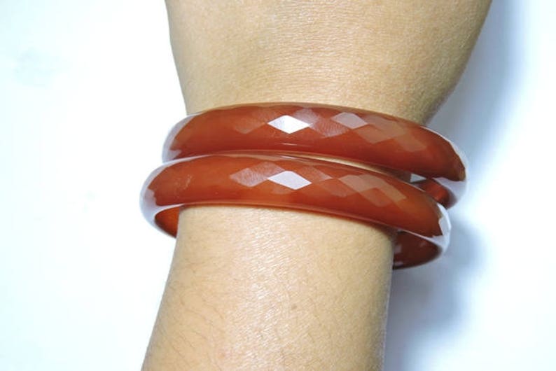 K&ouml;nnte beinhalten: Zwei braune, facettierte Armreifen, die auf dem Handgelenk einer Person &uuml;bereinander liegen.
