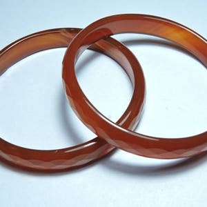 K&ouml;nnte beinhalten: Zwei rote Karneol-Armreifen mit einem facettierten Design.