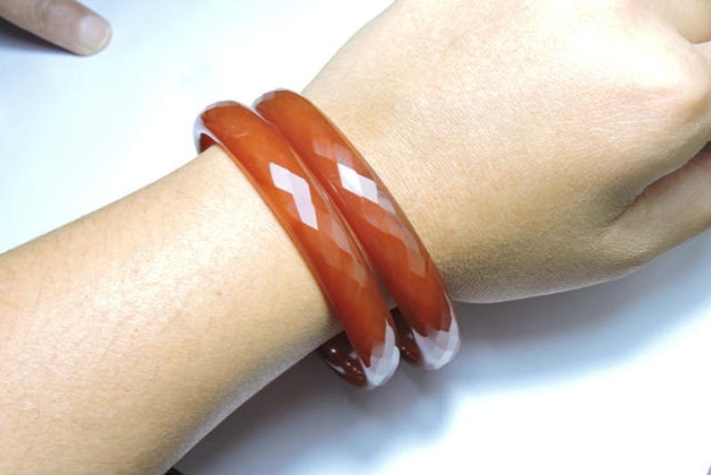 K&ouml;nnte beinhalten: Zwei braune Armreifen mit facettiertem Design. Die Armreifen werden am Handgelenk einer Person getragen.