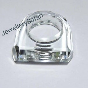 Puede incluir: Un porta anillos de cristal transparente con un dise&ntilde;o facetado. El porta anillos tiene forma de anillo y una base cuadrada.
