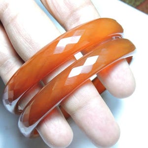 K&ouml;nnte beinhalten: Drei orangefarbene Armreifen mit Diamantmuster. Die Armreifen sind &uuml;bereinander gestapelt.