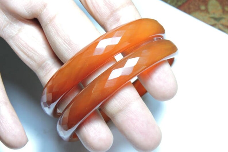 K&ouml;nnte beinhalten: Drei orangefarbene Armreifen mit Diamantmuster. Die Armreifen sind &uuml;bereinander gestapelt.