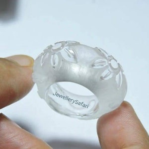 K&ouml;nnte beinhalten: Ein klarer, wei&szlig;er Ring mit einem floralen Design. Der Ring ist aus Wachs und wird von einer Hand gehalten. Der Text "JewellerySafari" ist auf dem Ring sichtbar.