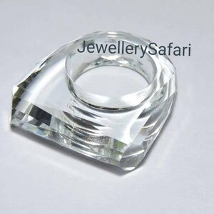 Puede incluir: Un porta anillos de cristal transparente con una base cuadrada y una parte superior redondeada. El porta anillos est&aacute; dise&ntilde;ado para sujetar un anillo de forma segura.