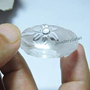 K&ouml;nnte beinhalten: Ein Ring aus klarem Quarz mit einem geschnitzten Blumendesign. Der Ring wird in einer Hand gehalten.