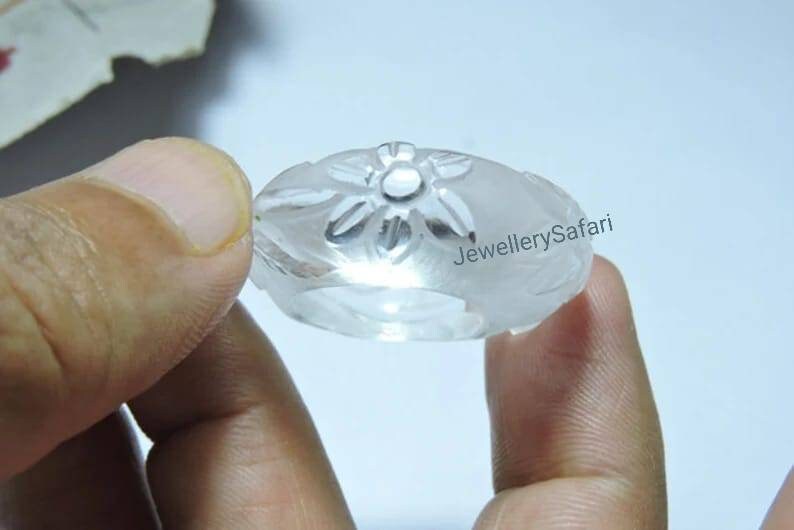 K&ouml;nnte beinhalten: Ein Ring aus klarem Quarz mit einem geschnitzten Blumendesign. Der Ring wird in einer Hand gehalten.