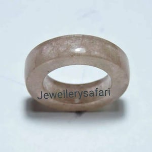 May include: A pale pink ring made of natural stone. The ring is smooth and has a simple design.